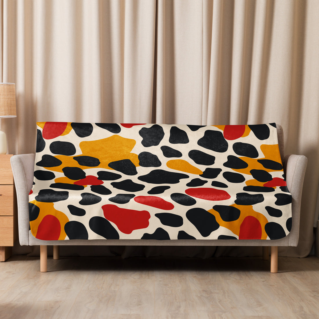 Sherpa blanket with vibrant leopard print design featuring red, yellow, and black abstract patterns draped over a couch.