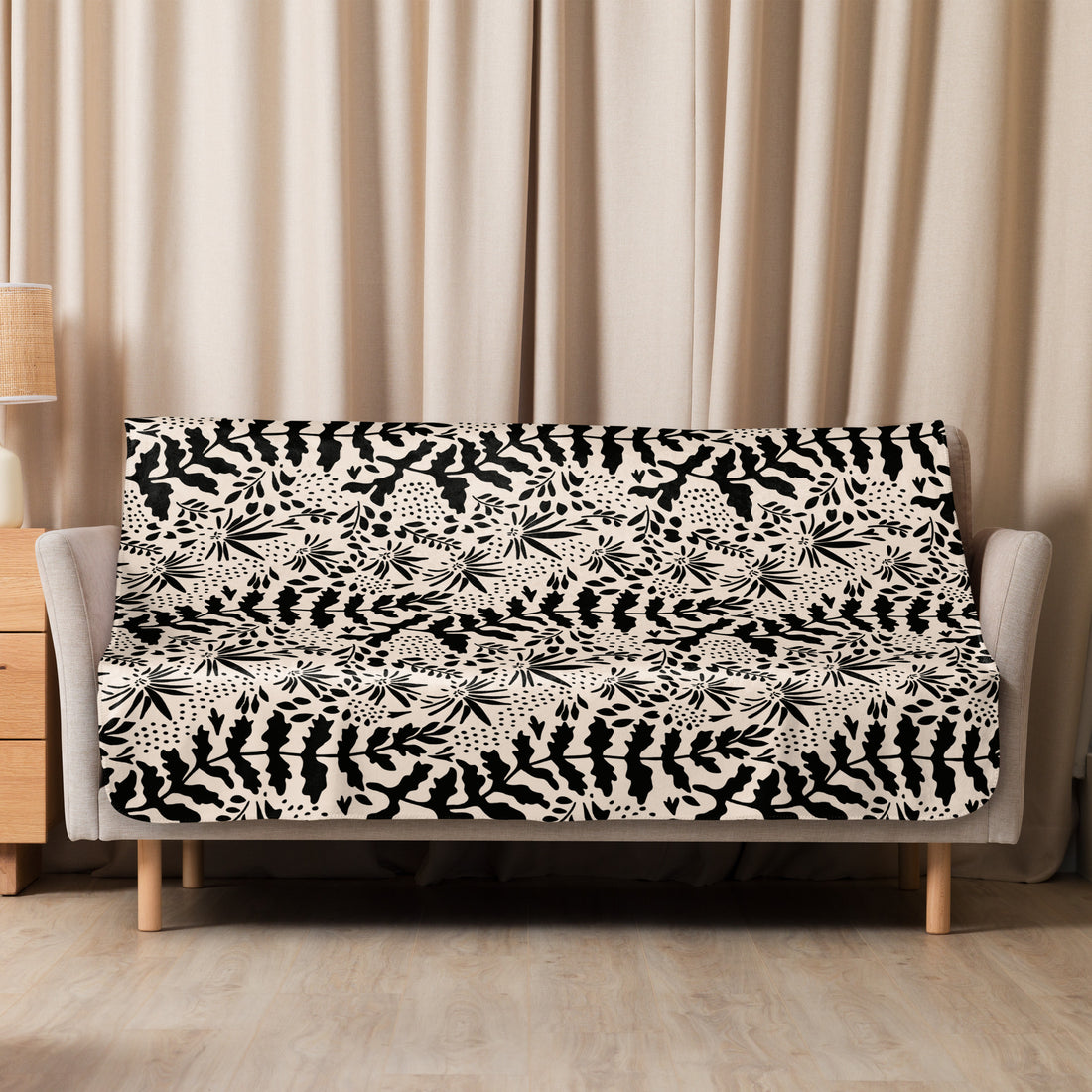 Sherpa blanket with intricate black floral patterns on a beige background, draped over a sofa, embodying elegance and warmth.