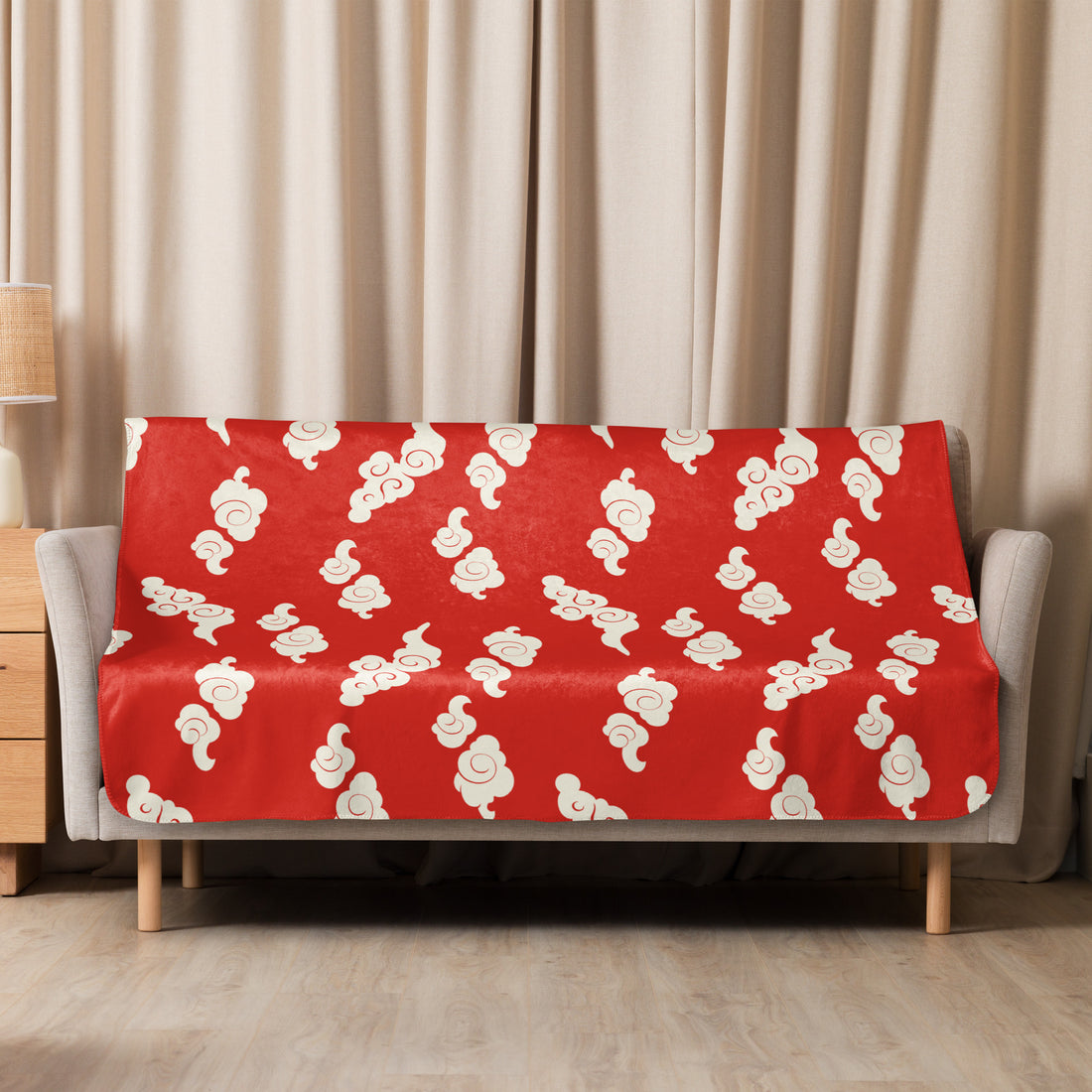 Red sherpa blanket with cream cloud pattern draped over sofa in cozy living room setting.