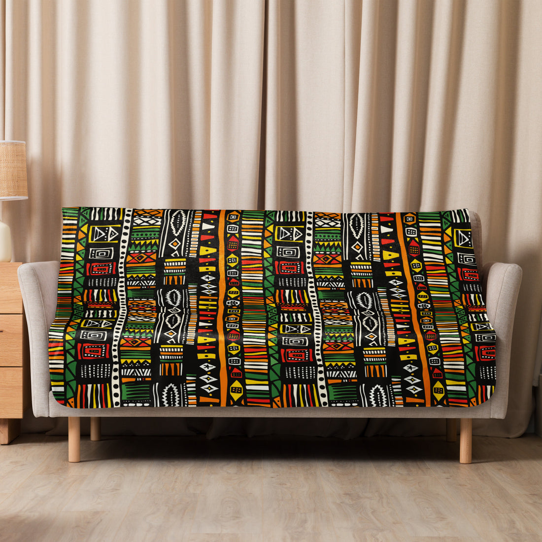 Tribal pattern sherpa blanket with vibrant African-inspired motifs in green, yellow, red, and black, draped over a beige couch, perfect for winter warmth and holiday coziness.