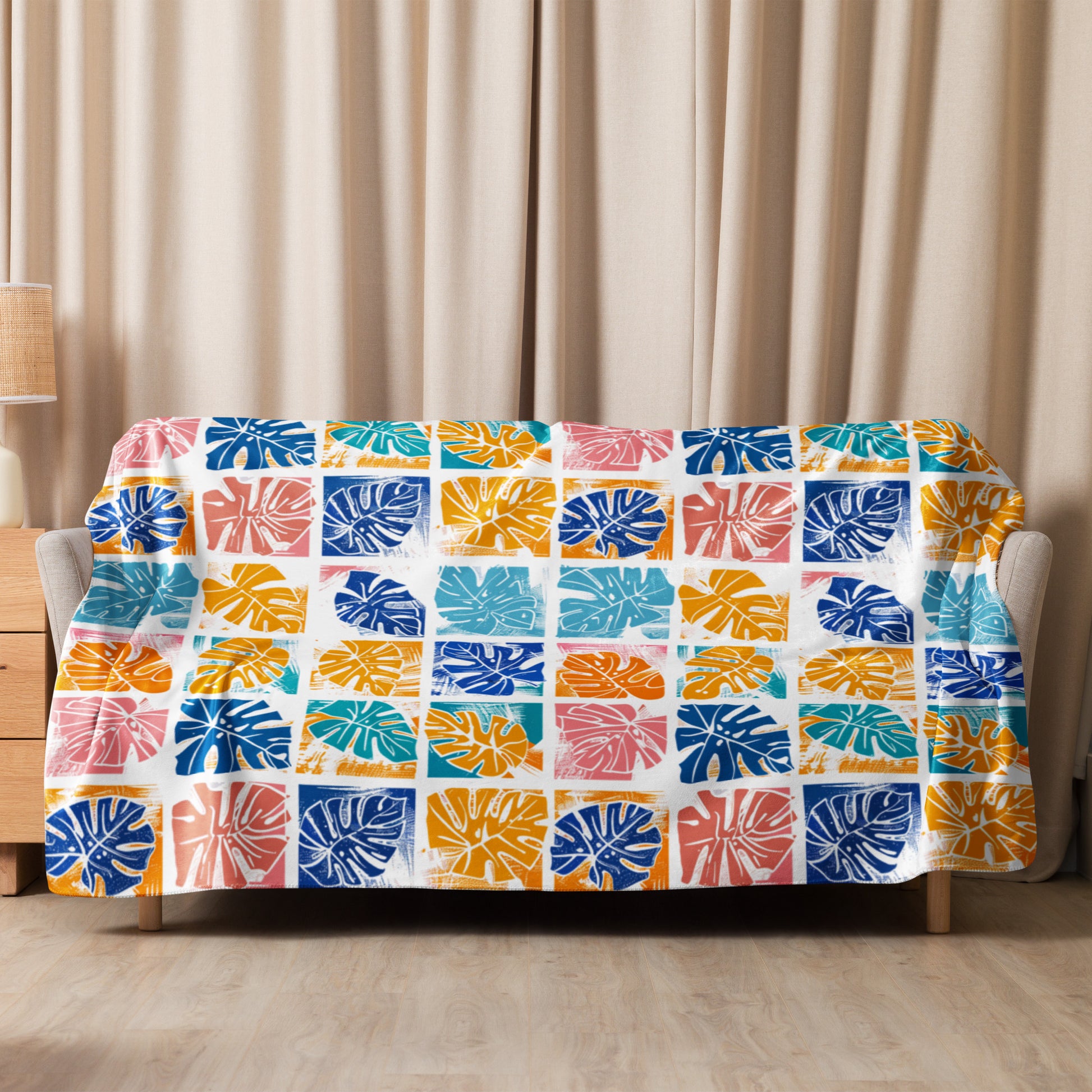 Colorful sherpa blanket with blue, orange, teal, and coral monstera leaf print draped over sofa