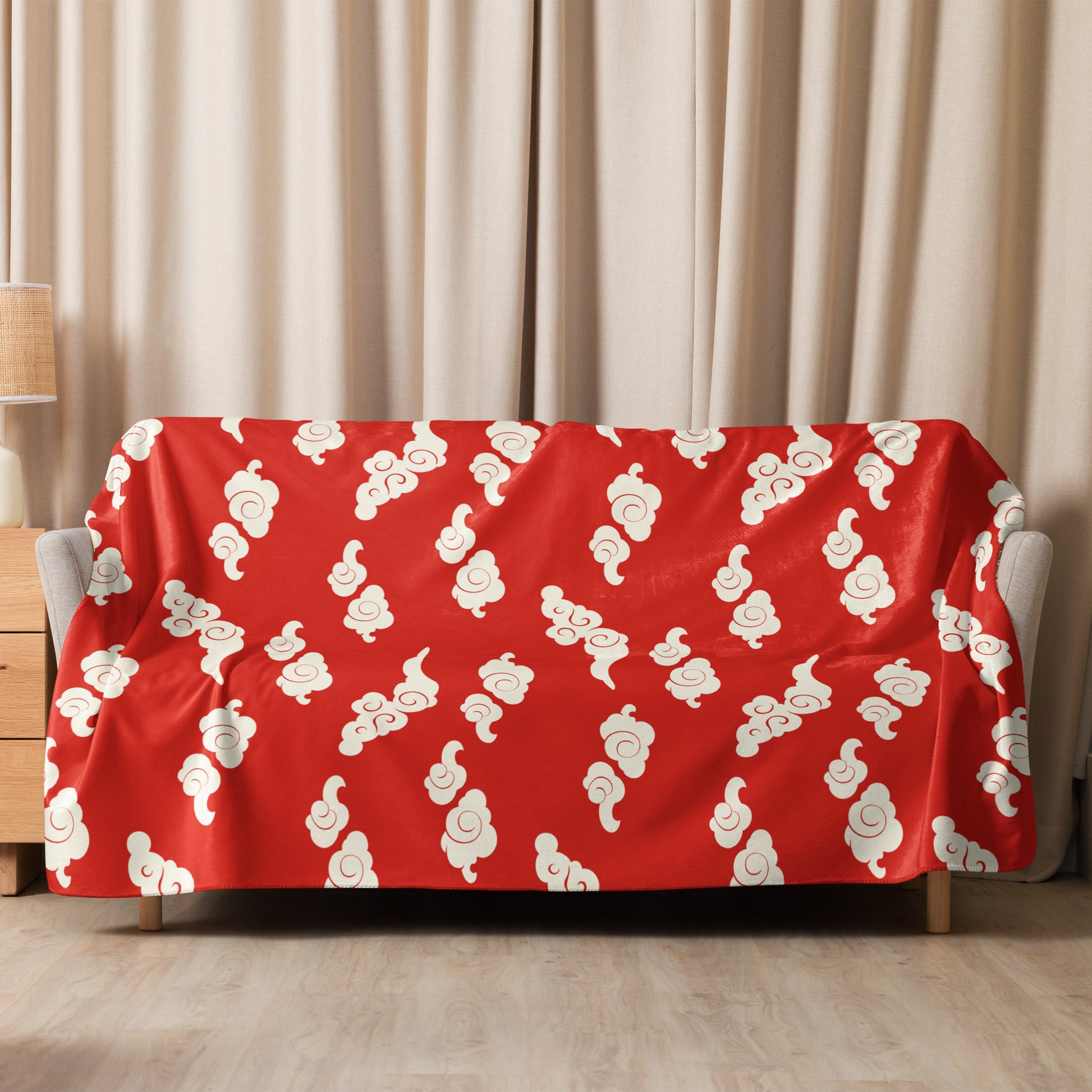 Red sherpa blanket with cream cloud pattern draped over sofa in cozy living room setting.