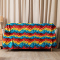 Colorful mandala pattern sherpa blanket draped over a couch, showcasing vibrant reds, blues, and yellows.