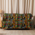 Tribal pattern sherpa blanket with vibrant African-inspired motifs in green, yellow, red, and black, draped over a beige couch, perfect for winter warmth and holiday coziness.