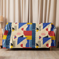 Sherpa blanket draped on a couch with an abstract geometric pattern in blue, red, yellow, and cream colors, adding a modern artistic touch.