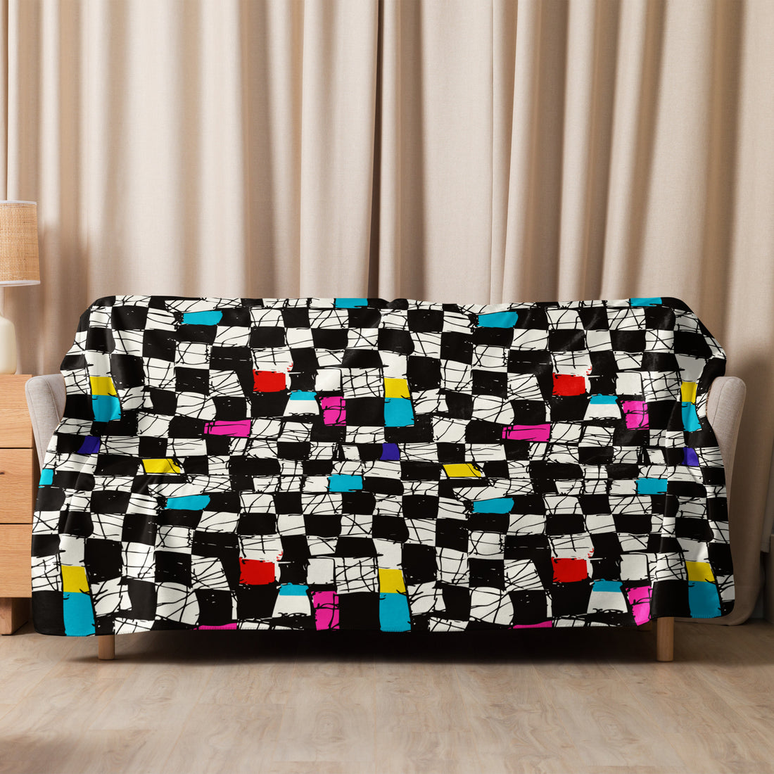 A sherpa blanket featuring a vibrant checkered design with splashes of red, blue, yellow, pink, and turquoise on a black and white background, draped over a couch.