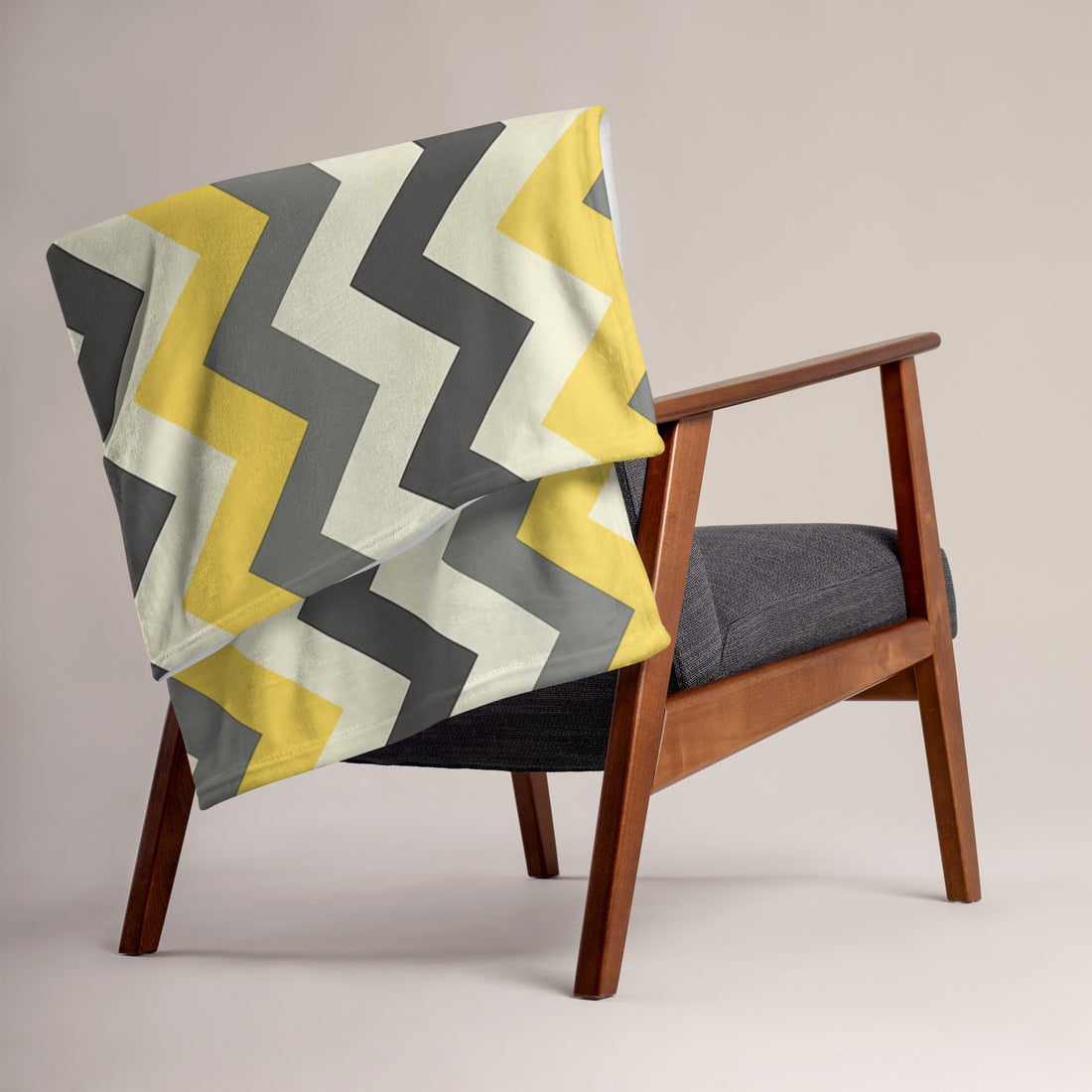 Chevron patterned throw blanket in grey and yellow on a modern chair. Soft silk touch fabric for cozy comfort.