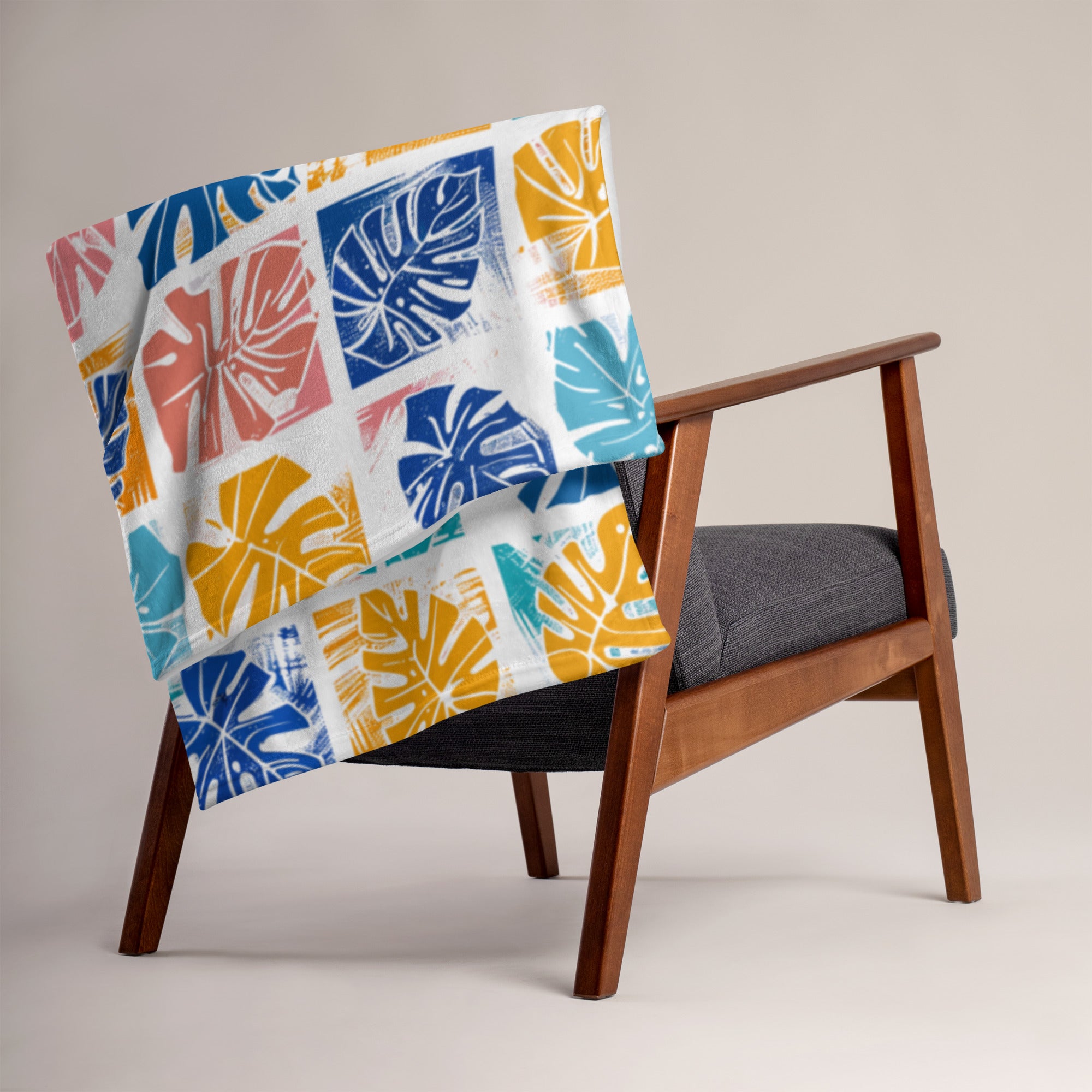 Colorful throw blanket featuring tropical monstera leaf design in orange, yellow, and blue on a wooden chair