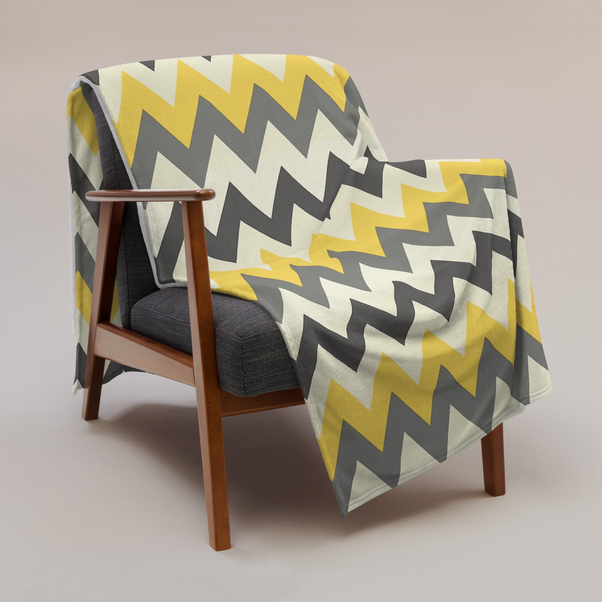 Chevron patterned throw blanket in grey and yellow on a modern chair. Soft silk touch fabric for cozy comfort.