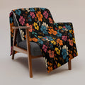 Vibrant floral silk touch throw blanket displayed on a modern armchair, featuring colorful flowers on a black background.