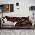 Cozy throw blanket with red floral pattern on a sofa, black background and white reverse side.