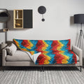 Vivid kaleidoscope pattern blanket in red, blue, and yellow hues draped over a sofa in a modern living room.