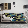 Knitted throw blanket with Nightfall Mosaic design in deep blues, greens, and yellows draped over a modern sofa.