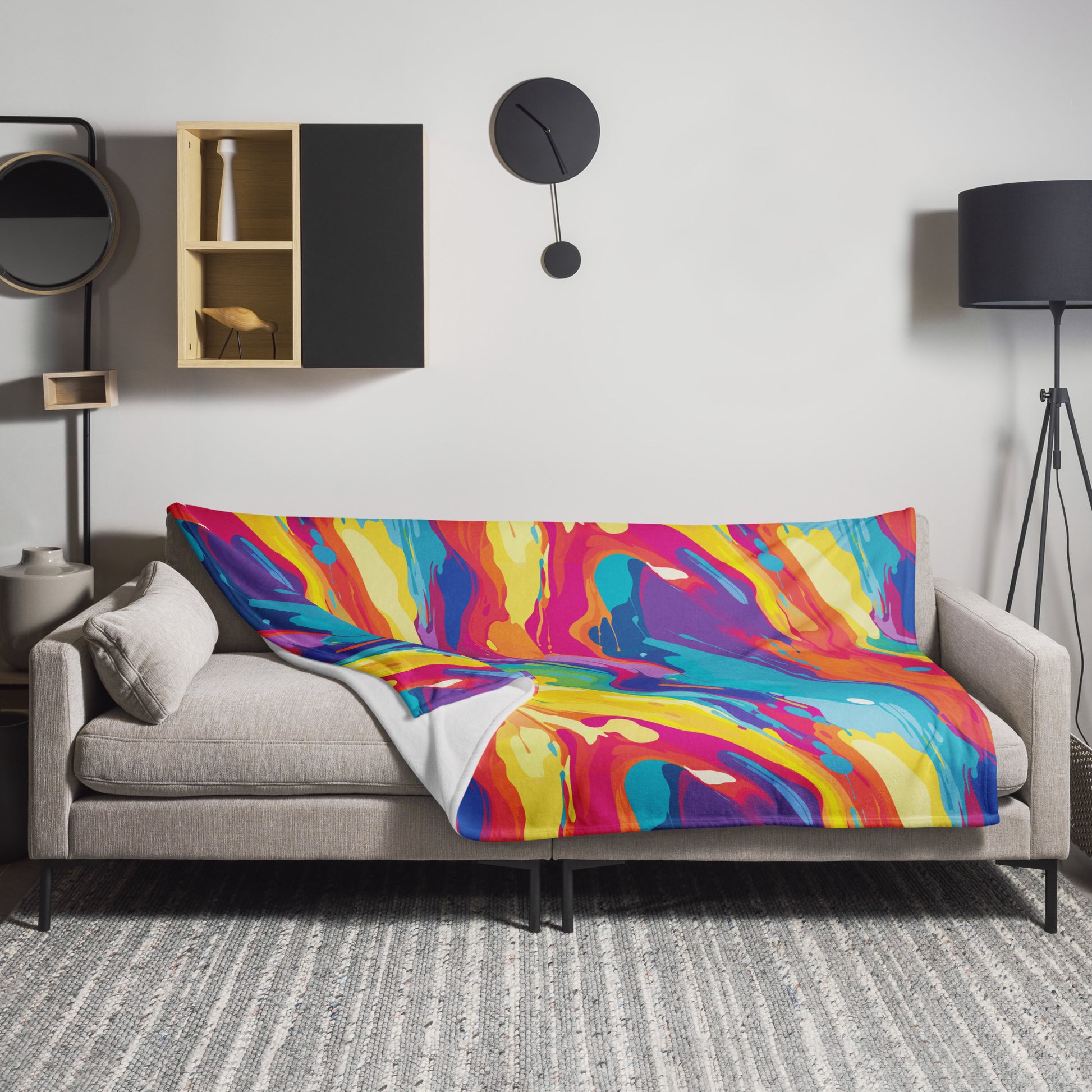 Vibrant Abstract Knitted Throw Blanket featuring bold swirls of pink, royal blue, and yellow, draped over a grey couch.