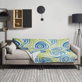 Swirling blue and green patterned throw blanket draped over a sofa, featuring a vibrant and cozy aesthetic.