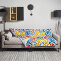 Colorful throw blanket with vibrant abstract figure design draped over a couch.